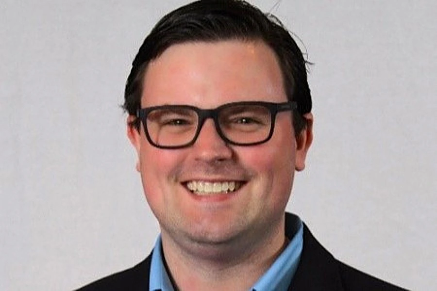 middle aged man in suit smiling with glasses against grey backdrop